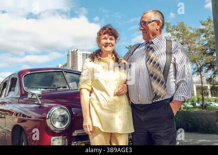 un homme âgé et une femme en promenade dans la ville dans une voiture vintage avec un bouquet de fleurs Banque D'Images