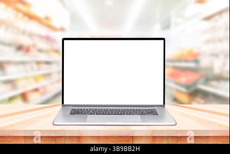 Ordinateur portable sur table avec fond de supermarché. Une maquette d'ordinateur portable à écran blanc et des accessoires sur un bureau blanc dans un supermarché moderne Banque D'Images