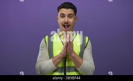 Jeune homme portant un gilet réfléchissant se tient contre un mur violet isolé en tant que bénévole pour un projet de service communautaire Banque D'Images