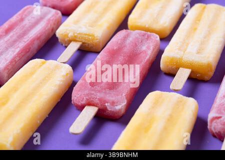 Popsicles rouges à la fraise et popsicles jaunes sur fond violet Banque D'Images