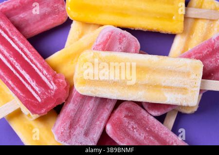 Popsicles rouges à la fraise et popsicles jaunes sur fond violet Banque D'Images