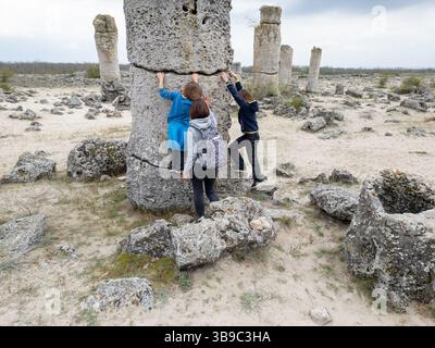 Mère et deux enfants explorent un terrain rocheux dans un paysage sec et semi-désertique. Les enfants jouent sur des formations de pierre pendant que la mère regarde, enjo Banque D'Images