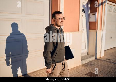 Technicien souriant marchant avec un ordinateur portable dans un quartier résidentiel Banque D'Images