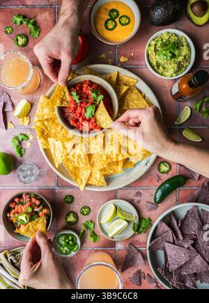 Vue de dessus mains avec frites, salsa, guacamole, boissons sur carrelage. Banque D'Images