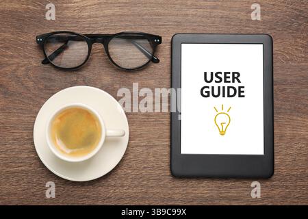 Guide de l'utilisateur document ouvert dans le dispositif e-book, tasse de café et lunettes sur la table en bois, pose à plat Banque D'Images