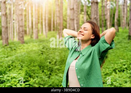 Femme heureuse debout avec les mains derrière la tête, appréciant la nature dans la forêt Banque D'Images