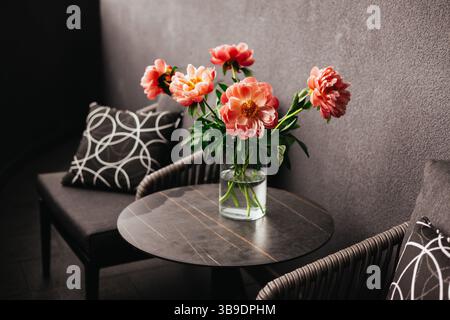 Une superbe disposition de pivoines corail dans un vase se trouve sur une table moderne avec des sièges confortables. Arrangement floral avec des fleurs printanières sur une table. Banque D'Images