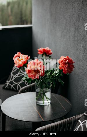 Une superbe disposition de pivoines corail dans un vase se trouve sur une table moderne avec des sièges confortables. Arrangement floral avec des fleurs printanières sur une table. Banque D'Images