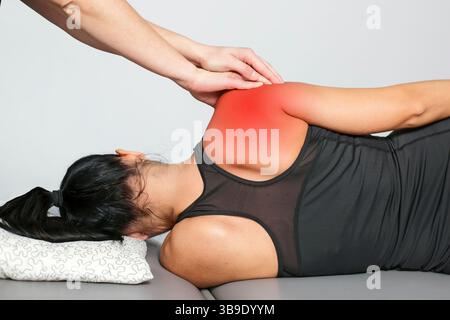 Séance de traitement des douleurs de l'épaule. Femme couchée sur le côté. Thérapeute touchant l'épaule rouge douloureuse. Récupération des blessures sportives. Réadaptation physiothérapeutique. Banque D'Images