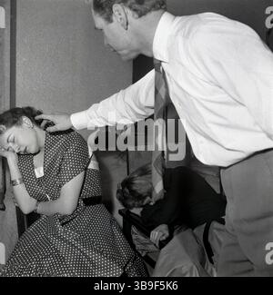 années 1950, historique, hypnose..... assis s'est affaissé sur une chaise une jeune femme dans une transe profonde de rêve après avoir subi l'hypnose par un praticien masculin. Une autre jeune femme s'est également effondrée dans une chaise en état de transe. Banque D'Images