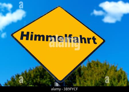 Allemagne - 9 mai 2025 : PHOTOMONTAGE, panneau jaune avec l'inscription : Ascension, devant un ciel bleu *** FOTOMONTAGE, Gelbes Schild mit der Aufschrift : Himmelfahrt, vor blauem Himmel Banque D'Images