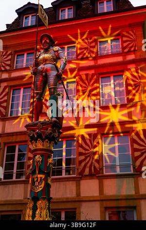 Fontaine avec statue devant une maison illuminée dans la vieille ville dans un crépuscule dans la ville de Neuchâtel, Canton Neuchâtel, Suisse. Banque D'Images