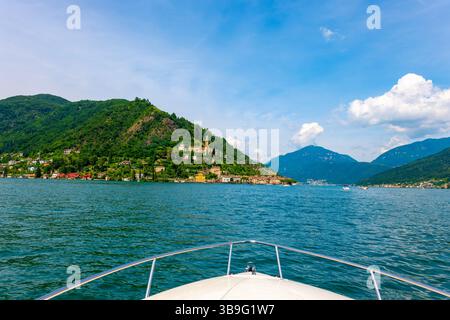 Vue depuis un bateau à moteur sur le lac de Lugano et Maison et église sur la chaîne de montagnes dans une journée d'été ensoleillée sur le front de mer à Morcote, Lugano, Tessin, Switze Banque D'Images