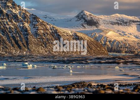 Une superbe scène hivernale islandaise capture les sommets enneigés de Skaftafell dispersés sur un plan d'eau tranquille, mettant en valeur la beauté brute an Banque D'Images