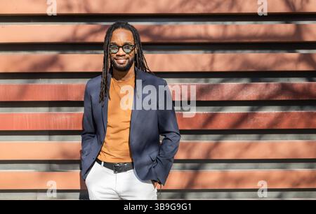 Un homme d'affaires cubain avec des dreadlocks, portant des lunettes de soleil, respire la confiance dans un blazer bleu, une chemise moutarde et un pantalon blanc. Il se penche désespérément Banque D'Images