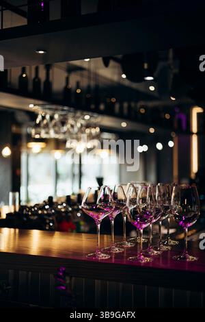 Une collection de verres vides élégamment alignés sur un comptoir de bar, éclairés par un éclairage ambiant et chaleureux. La scène définit un sophistiqué et invitant Banque D'Images