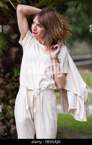 Femme dans une tenue blanche élégante apprécie le plein air frais. Avec une pose décontractée, elle regarde sur le côté, ses cheveux doucement émoussés par la brise, rayonnant Banque D'Images