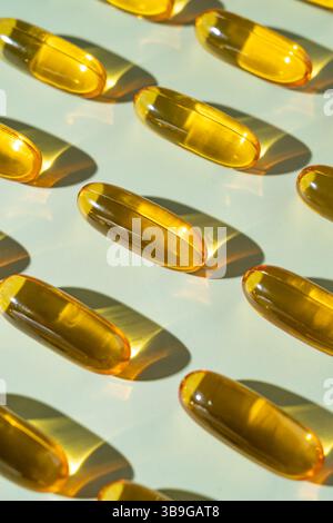 Plusieurs capsules Oméga 3 disposées soigneusement sur un fond clair, réfléchissant la lumière du soleil. Les capsules de gel sont translucides et dorées, mettant en valeur leurs Banque D'Images