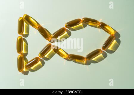 Vue de dessus de capsules d'acides gras oméga 3 dorées artistiquement disposées dans une boucle circulaire ressemblant à un poisson sur un fond vert doux, mettant l'accent sur Heal Banque D'Images