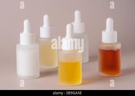 Cette image présente une collection de cinq flacons compte-gouttes translucides avec des liquides de différentes couleurs sur un fond beige doux, idéal pour le bien-être et Banque D'Images