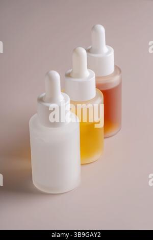 Trois flacons compte-gouttes gradués avec différents contenus affichés sur un fond beige neutre. Parfait pour mettre en valeur les produits de soin de la peau ou de bien-être Banque D'Images