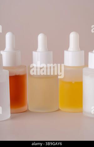 Une collection soigneusement arrangée de flacons compte-gouttes remplis de liquides dans les tons ambre, beige et jaune, serrés contre un fond beige complémentaire Banque D'Images