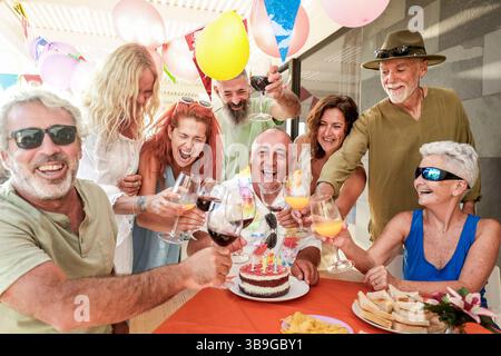 Joyeux groupe d'amis réunis autour d'une table célébrant un anniversaire avec un gâteau et des boissons. Les décorations et les ballons créent une ambiance festive ou Banque D'Images