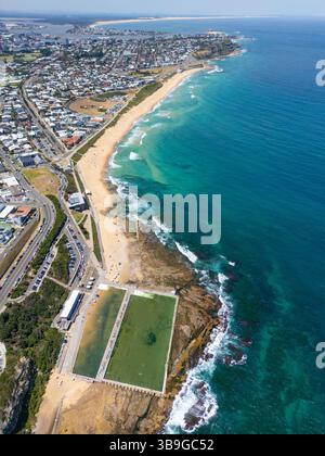 Image d'une grande piscine océanique construite le long de la côte rocheuse de Newcastle, avec plage dorée, eau turquoise claire, et développement urbain à proximité à ne Banque D'Images