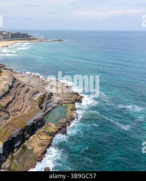 Piscine rocheuse naturelle le long des falaises de la côte de Newcastle, avec des vagues turquoises, un terrain accidenté et des plages de sable lointaines en Nouvelle-Galles du Sud, Australie Banque D'Images