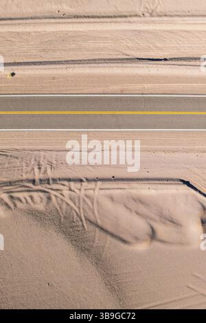 Vue aérienne d'une route asphaltée droite traversant un paysage désertique sablonneux de la Puna argentine. La route est accompagnée de motifs complexes i Banque D'Images