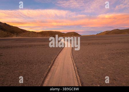 Une scène désertique tranquille présente un chemin sinueux sous un magnifique coucher de soleil dans la Puna argentine. Le ciel est peint avec des teintes de rose et d'orange, créati Banque D'Images