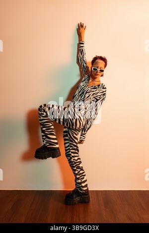 Une jeune femme élégante pose en toute confiance contre le mur dans un ensemble audacieux à imprimé zèbre. Elle dégage une ambiance moderne et avant-gardiste avec son choix de s surdimensionnés Banque D'Images