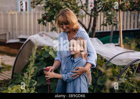 Un joyeux duo mère fille tend à leur serre, entouré de plantes luxuriantes. Ils partagent un lien spécial tout en arrosant les légumes sous le W. Banque D'Images