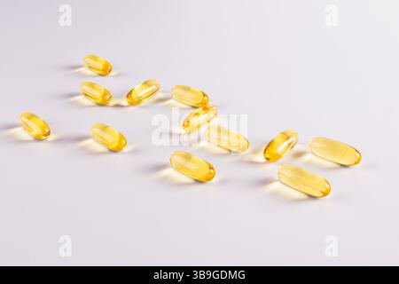 Gros plan des gélules d'oméga 3 et de vitamine E sur fond blanc. Les capsules jaunes brillantes sont dispersées, soulignant leur texture translucide Banque D'Images