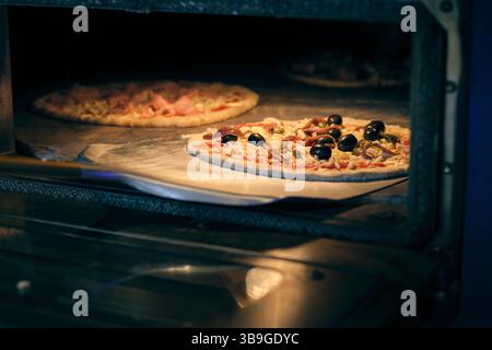 Deux pizzas cuites dans un four professionnel, avec mozzarella, olives, câpres et autres garnitures Banque D'Images