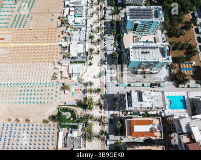 Photographie aérienne du front de mer animé de San Benedetto avec des rangées organisées de parasols colorés, des bâtiments adjacents et des rues bordées de palmiers. PE Banque D'Images