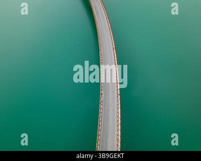 Vue aérienne d'un pont gracieusement courbé sur les eaux sereines et turquoises du lac Castreccioni, Italie. L’arc élégant du pont contraste avec le c Banque D'Images