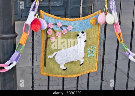 Décoration tricotée sur une clôture montrant un paysage avec un mouton, des fleurs et des œufs de Pâques, accroché avec une chaîne tricotée colorée à Ripon, Yorkshire, Royaume-Uni. Banque D'Images