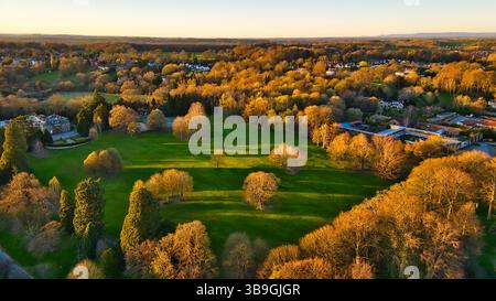 Vue aérienne d'un champ verdoyant avec des arbres, des bâtiments et des maisons lointaines sous un ciel clair, illuminé par la lumière dorée du soleil à Knaresborough, Royaume-Uni. Banque D'Images