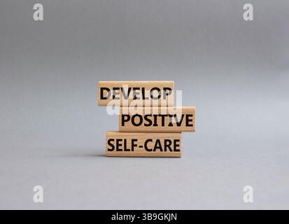 Développez un symbole d'autosoins positif. Les mots conceptuels développent un autosoin positif sur les blocs de bois. Beau fond gris. Affaires et développement positif Banque D'Images