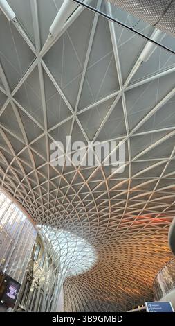 Une prise de vue en angle bas met en valeur le plafond géométrique complexe d'un bâtiment, avec des motifs triangulaires et des poutres métalliques. Banque D'Images