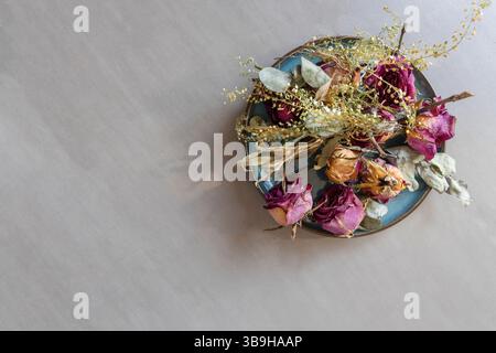 Les pétales de rose séchés se trouvent comme un arrangement floral coloré sur une assiette turquoise Banque D'Images
