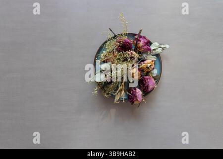 Les pétales de rose séchés se trouvent comme un arrangement floral coloré sur une assiette turquoise Banque D'Images