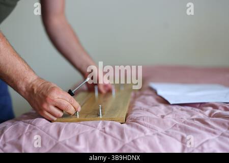 main de l'homme à l'aide d'un tournevis manuel et d'une vis de vissage dans le panneau du tiroir pour la charnière de rail. Assemblage de nouveaux meubles en bois. Gros plan. Banque D'Images