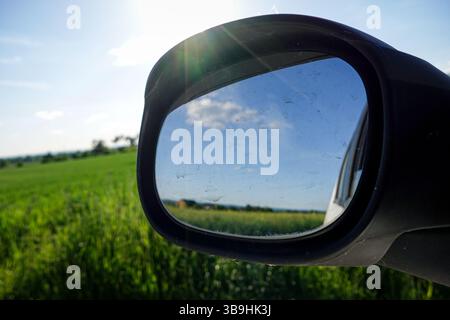 Le rétroviseur d'une voiture montre un champ avec un ciel bleu. Le miroir est sale et a un reflet du ciel Banque D'Images