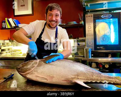 Oskar Rossi, chef du restaurant primé Fico, portant des gants et un tablier filetant un thon entier sur le banc de préparation de son restaurant Banque D'Images