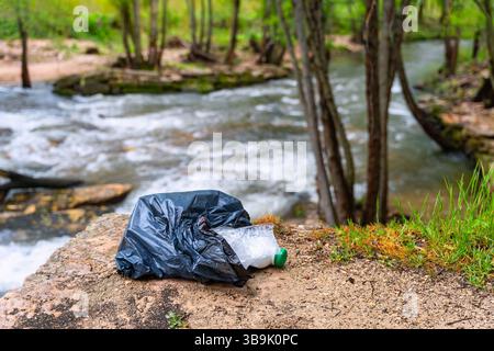 Sac poubelle avec des ordures et des restes de plastique jetés par la rivière au milieu de la nature. Banque D'Images