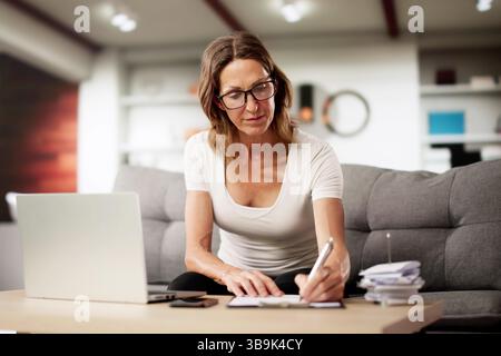 Femme travaillant sur les finances en ligne de canapé à la maison. Professions possibles : Conseiller financier en ligne Banque D'Images