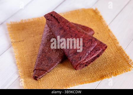 Gros plan de deux morceaux de pastille de fruits triangulaires rouges pliés reposant sur un tissu jaune montrant des détails de texture de surface Banque D'Images