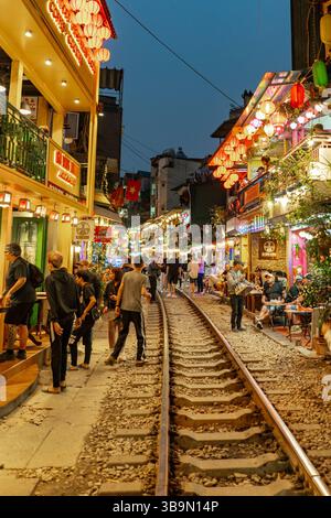 Une scène nocturne animée se déroule le long de la rue de train de Hanoi, remplie de gens et d'une atmosphère animée. La rue est éclairée par des lanternes décoratives. Banque D'Images